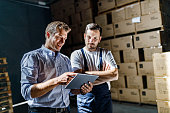 Happy inspector using digital tablet with warehouse worker in a storage room.