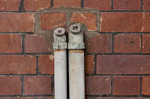 Old brown metal pipes down a brick wall.