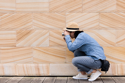 Woman outdoors against a sandstone wall taking a photo with her camera.