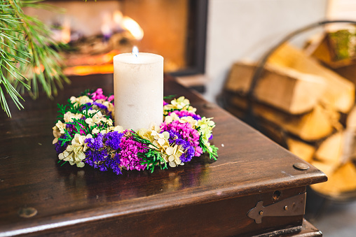 Handle lighting a candle. In a beautiful, hand made wreath. On an old wooden table in front of a fireplace.