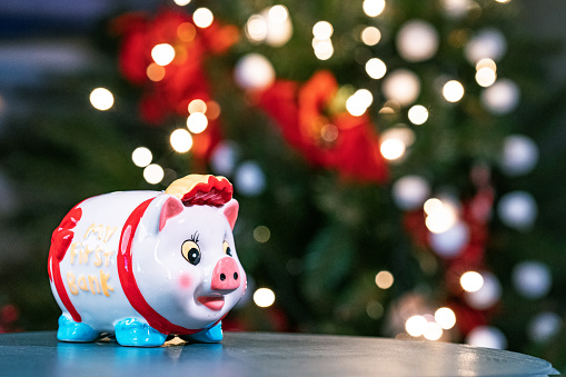 christmas piggy bank ball with ribbon bow on red blurred lights background sale concept