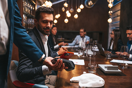 Business people paying the restaurant check using mobile contactless payments after a meeting.