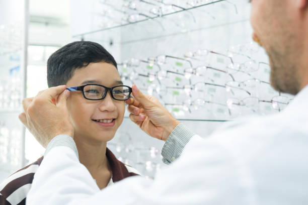 menino inteligente experimentando novos óculos. - eye exam optometrist eyesight human eye - fotografias e filmes do acervo