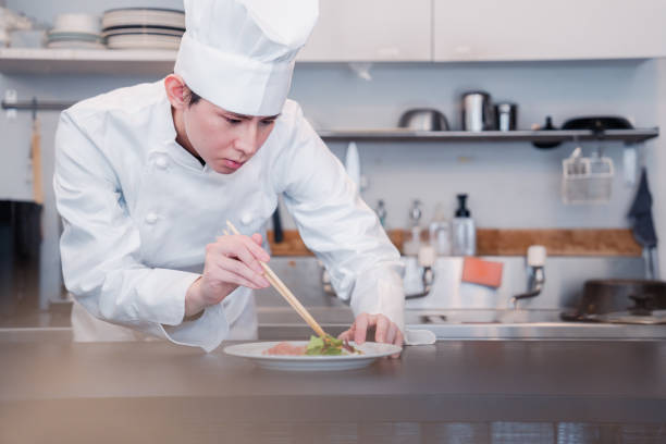 This photo shows fresh shrimp and calamari prepared in front of a chef in a kitchen. The shrimp and calamari are placed on a white plate and surrounded by some parsley and other herbs. The chef is blurred in the background and is presumably about to prepare the dish. This is a great photo to use for photos about cooking, fresh produce, and seafood.