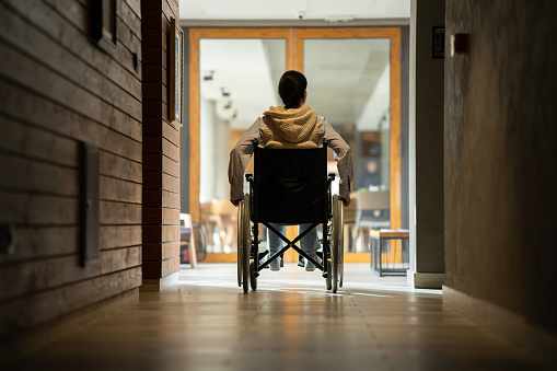 Young woman sitting in wheelchair and moving down the building hallway