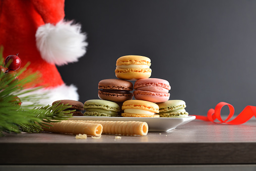 Stack of various flavors french macaroons served on white plate on wooden table with dark background with santa hat. Front view.
