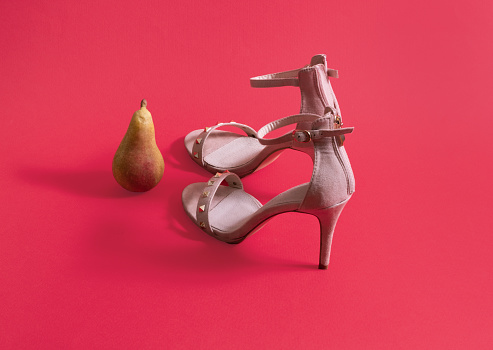 Pear and pair of high heels on pastel red background. Minimal horizontal composition, modern woman lifestyle concept