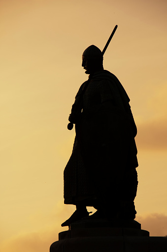 Guimarães, Portugal- May 3, 2011: Statue of Dom Afonso Henriques silhouetted at dusk,  gold colored sky background, Dukes de Braganca Palace nearby. Guimarães, Portugal.