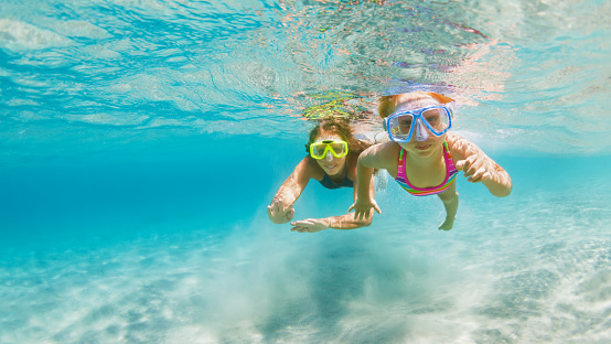 Young mother with child in snorkeling mask dive in coral reef sea lagoon to explore underwater world. Family travel lifestyle in summer adventure camp. Swimming activities on beach vacation with kids.