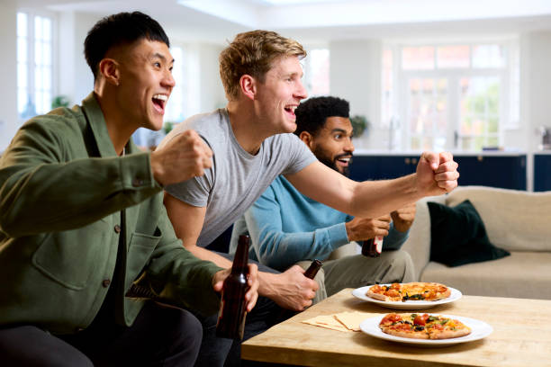 group of excited male friends watching sports on tv at home in lounge with pizza together - fan sport football male imagens e fotografias de stock