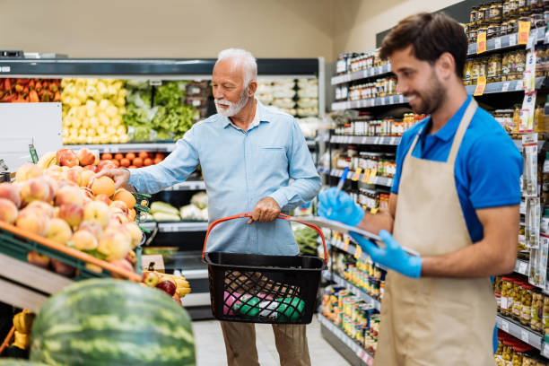 istock Employee in supermarket arranging fresh fruit and serving senior customer 1445979008