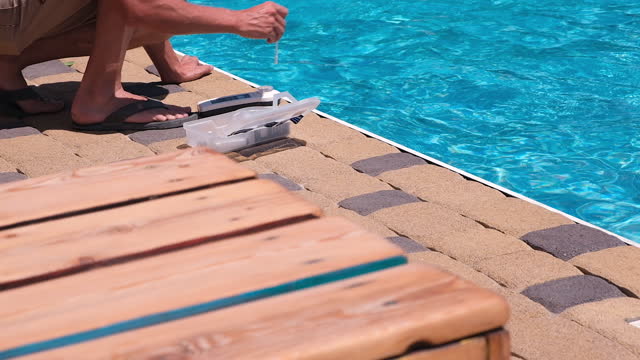 A man will check the quality of the water. Checking the quality of pool water with a chemical test kit in summer. pH, Chlorine and Bromine Concentration. Water pool SPA. Maintenance. 4k. Slow Motion