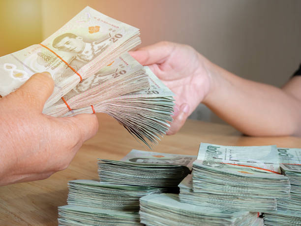 istock Handing over stacks of Thai banknote to other hand with soft light background. 1445979589