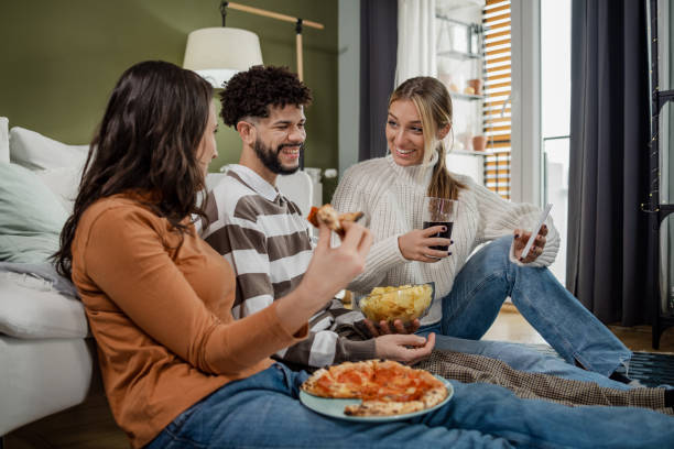 Relaxed and friendly atmosphere Group of friends having a joyful weekend. They are sitting on the floor, eating, drinking and talking. family eating potato chips stock pictures, royalty-free photos & images