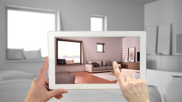 istock Augmented reality concept. Hand holding tablet with AR application used to simulate furniture and design products in total white unfinished background, cosy living room 1445981257