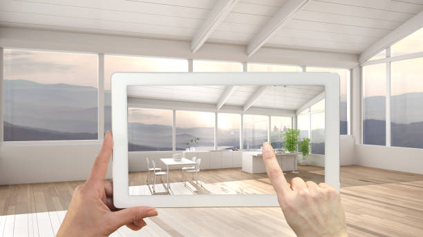 istock Augmented reality concept. Hand holding tablet with AR application used to simulate furniture and design products in empty interior with parquet, kitchen with island and dining table 1445981378