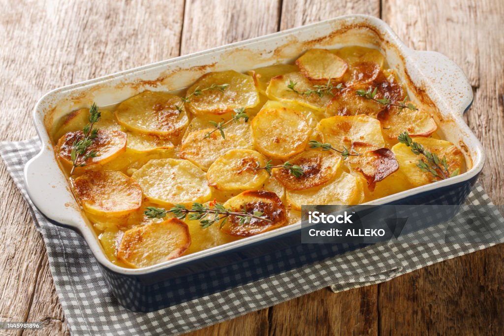 Scalloped potatoes, potato casserole with the addition of herbs, onion and garlic in a ceramic baking dish closeup. Horizontal Scalloped potatoes, potato casserole with the addition of herbs, onion and garlic in a ceramic baking dish closeup on the table. Horizontal Prepared Potato Stock Photo