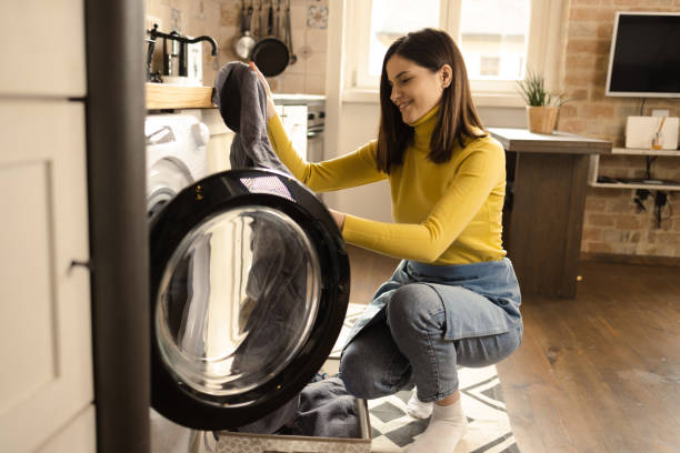 istock Happy young woman putting dirty laundry into a washing machine 1445982010
