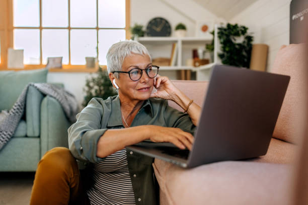 mujer mayor usando computadora portátil en el piso de la sala de estar - banca electrónica fotografías e imágenes de stock