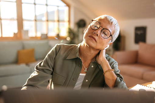 Overworked senior woman experiencing neck pain while working from home office