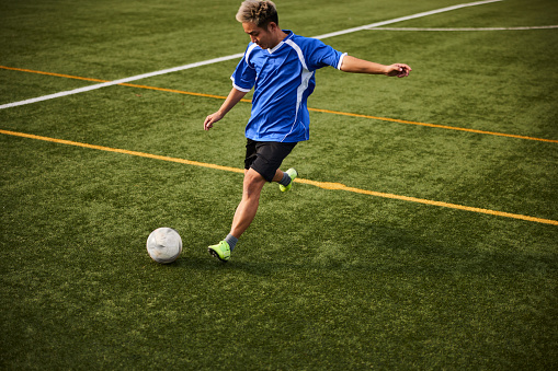 Full length portrait of professional soccer player kicking ball in motion against white background on green grass. Looks extremely motivated. Concept of game, sport, recreation, active lifestyle.