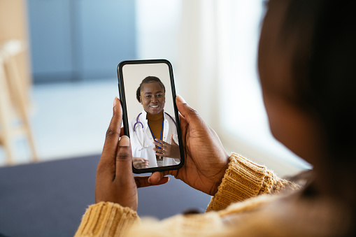 African woman using digital device, talking to doctor on video call