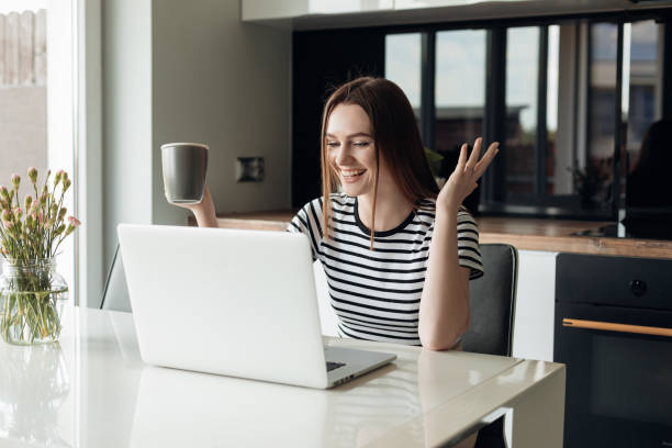istock Young laughing and cheerful female using white laptop and drinking coffee. Video call webinar, conference, remote job 1445986824