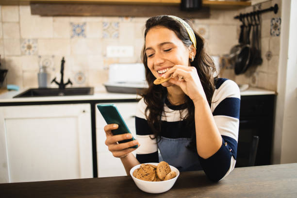 retrato de uma menina bonita que se diverte on-line enquanto petisca biscoitos - cookie women eating beautiful - fotografias e filmes do acervo