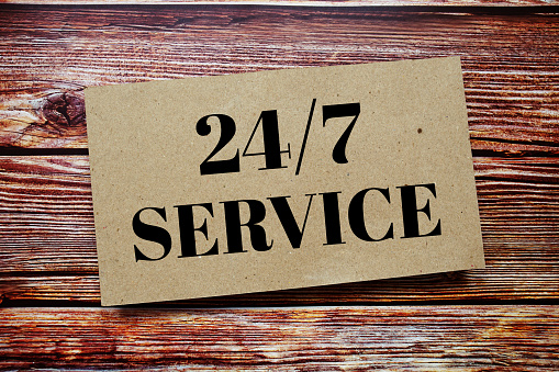 24 Hrs 7 Days Service written on paper card top view of wooden background