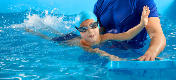 istock Trainer teaching little boy how to swim in indoor pool with pool floating board 1445991711