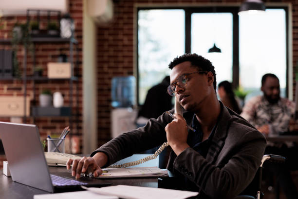istock Company employee with physical disability talking on landline phone 1445993003