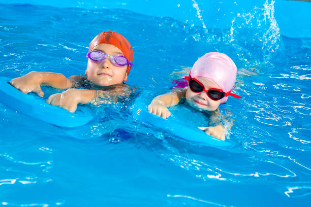 istock Two little girls having fun in pool learning how to swim using flutter boards 1445994048