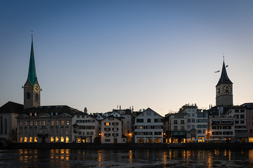 Dusk on the banks of the Limmat River seen from Limmatquai in Zurich, Switzerland. Highlighting the towers of Kirche Fraumünster and St. Peter's Church