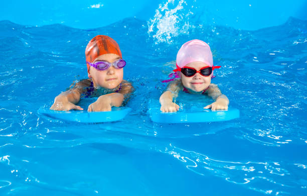 istock Two little girls having fun in pool learning how to swim using flutter boards 1445994584