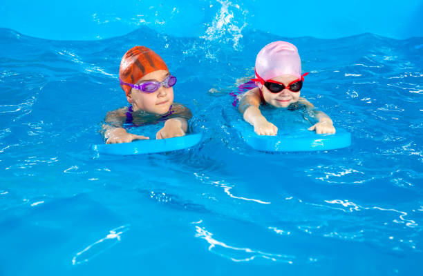 istock Two little girls having fun in pool learning how to swim using flutter boards 1445994909