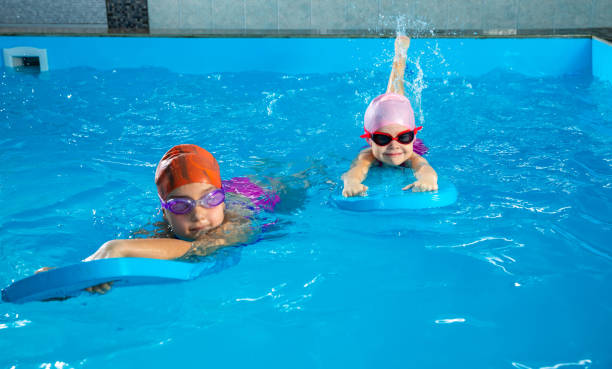 istock Two little girls having fun in pool learning how to swim using flutter boards 1445995071