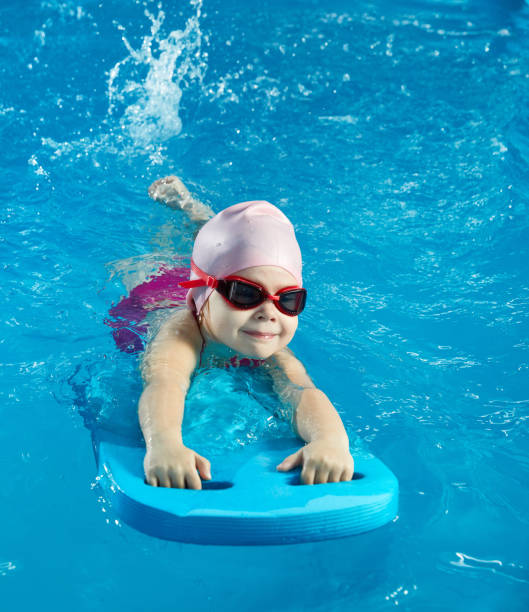 Little girl learning to swim in indoor pool with pool board stock photo