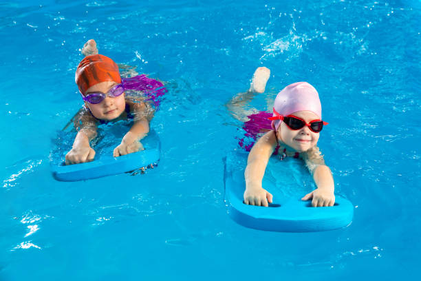 Two little girls having fun in pool learning how to swim using flutter boards stock photo