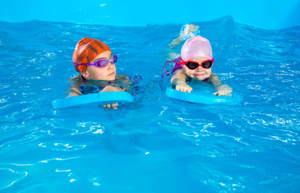 istock Two little girls learning how to swim in swimming pool using flutter boards 1445995997