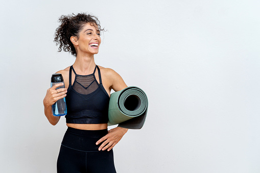 Woman smiling in front of white wall with mat and water bottle
