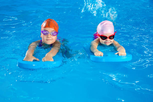 istock Two little girls learning how to swim in swimming pool using flutter boards 1445997043