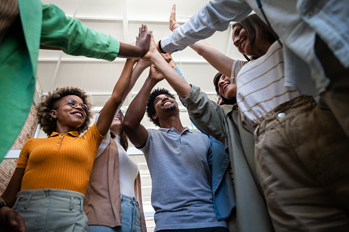 Group of multiracial coworkers join hands together in the air celebrating teamwork success. High five in the office. Business concept.