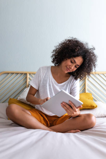 istock Young multiracial woman using sitting on bed down relaxing at home cozy bedroom. Vertical 1445997329