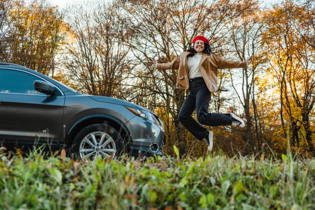 happy smiling woman in a red beret is jumping near the car on the background of autumn trees happy smiling woman in red beret is jumping near car on background of autumn trees hopper car stock pictures, royalty-free photos & images
