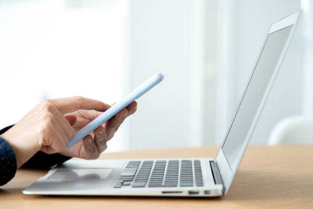 istock Side view of woman hands using mobile phone while working in the office with laptop. Blurred background. 1445997695