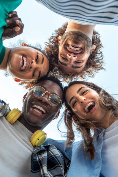 Low angle view of multiracial friends heads in circle. College student friends smiling looking at camera. Low angle view of multiracial friends heads in circle. College student friends smiling looking at camera. Friendship and team spirit concept. head shoot stock pictures, royalty-free photos & images