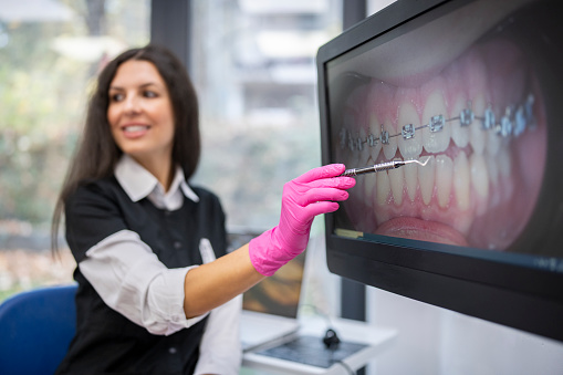 Smiling orthodontist assistant showing a photo of teeth with dental braces on screen.