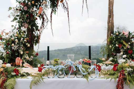 Beautiful rustic theme outdoor wedding white altar setup, wedding sand ceremony vases pouring glass lined up with natural flower decoration and mountain background.