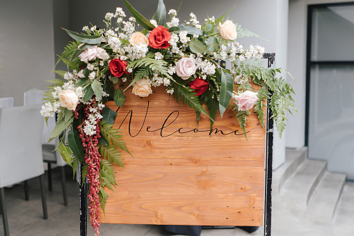 A welcome board sign with a beautiful flower decoration, standing in front of wedding entrance.