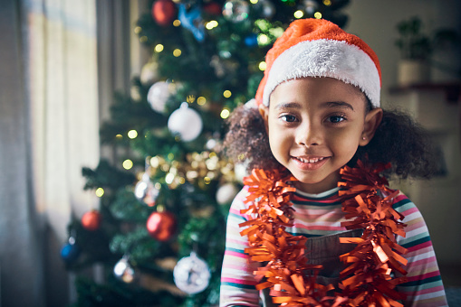 Christmas, happy and girl kid in holiday portrait, celebrate at home with hat and decoration, festive and tradition in living room. Smile, African American child and Christmas tree with happiness.
